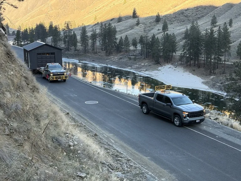 Clearwater Barns transporting a garage along a riverside road with an oversize-load escort truck